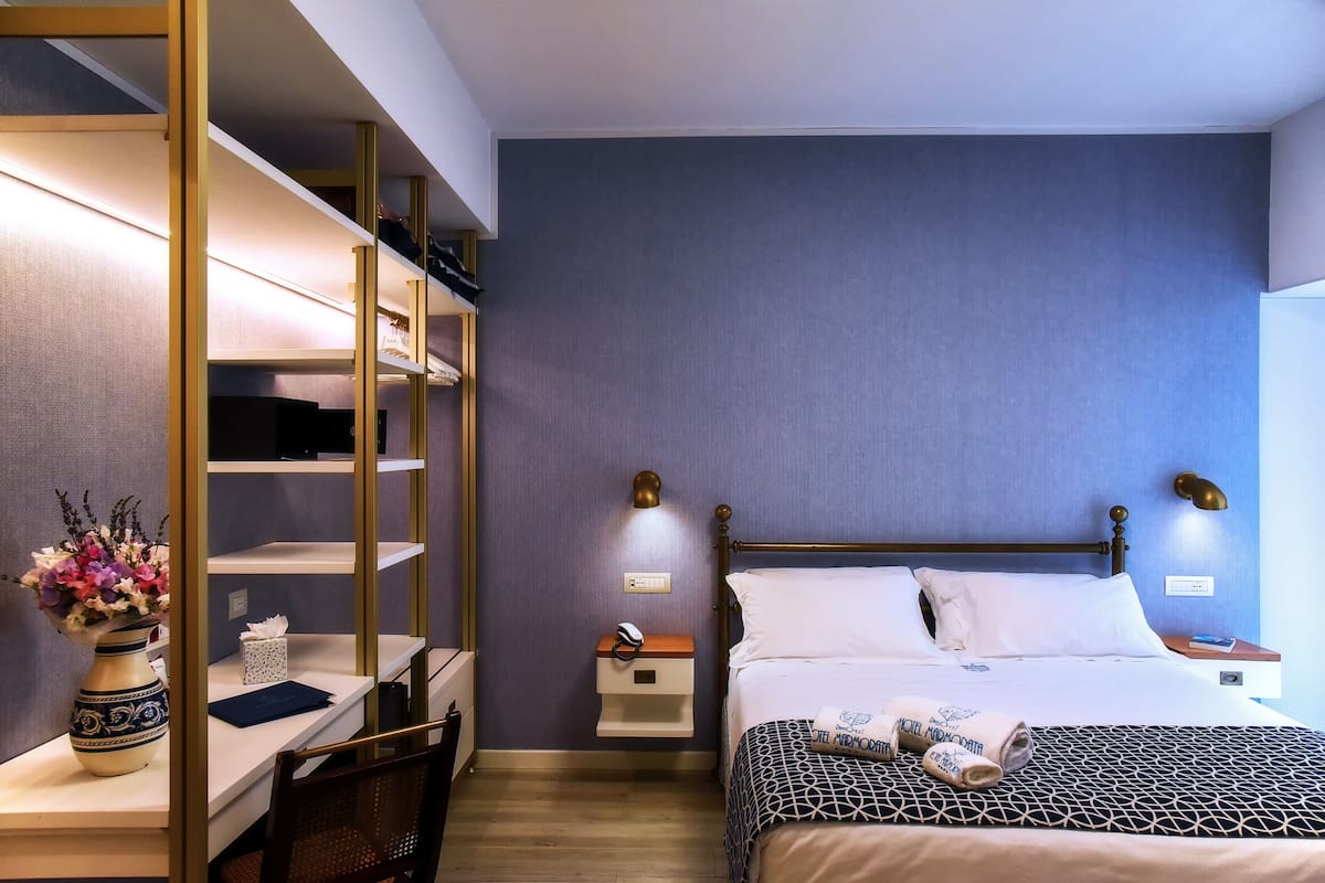 A hotel room with a bed, bedside tables, a desk, and a chair.