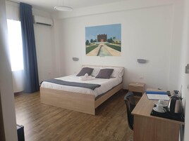 Una camera d'albergo con un letto, una scrivania con bollitore, tazze e telecomando.