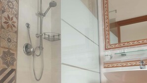 Un baño con ducha envuelta en vidrio, un lavamanos blanco y un espejo decorativo.