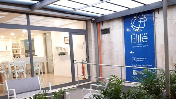 Vestíbulo de hotel con techo de vidrio, recepción, zona de estar y plantas en macetas.