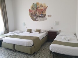 A hotel room with three beds, a patterned floor, a wall mural, and a small wooden nightstand.