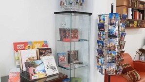 Una habitación con una vitrina de vidrio que contiene libros y postales, una mesa de madera con libros y un sofá rojo.