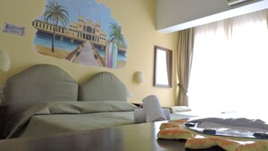Una habitación de hotel con cama, una mesa y un plato, un mural en la pared y una ventana.