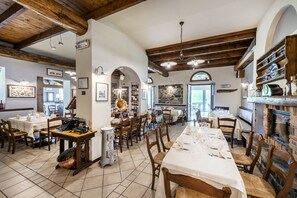 Un restaurante con vigas de madera, paredes de piedra y chimenea. Las mesas están preparadas con manteles blancos y sillas.