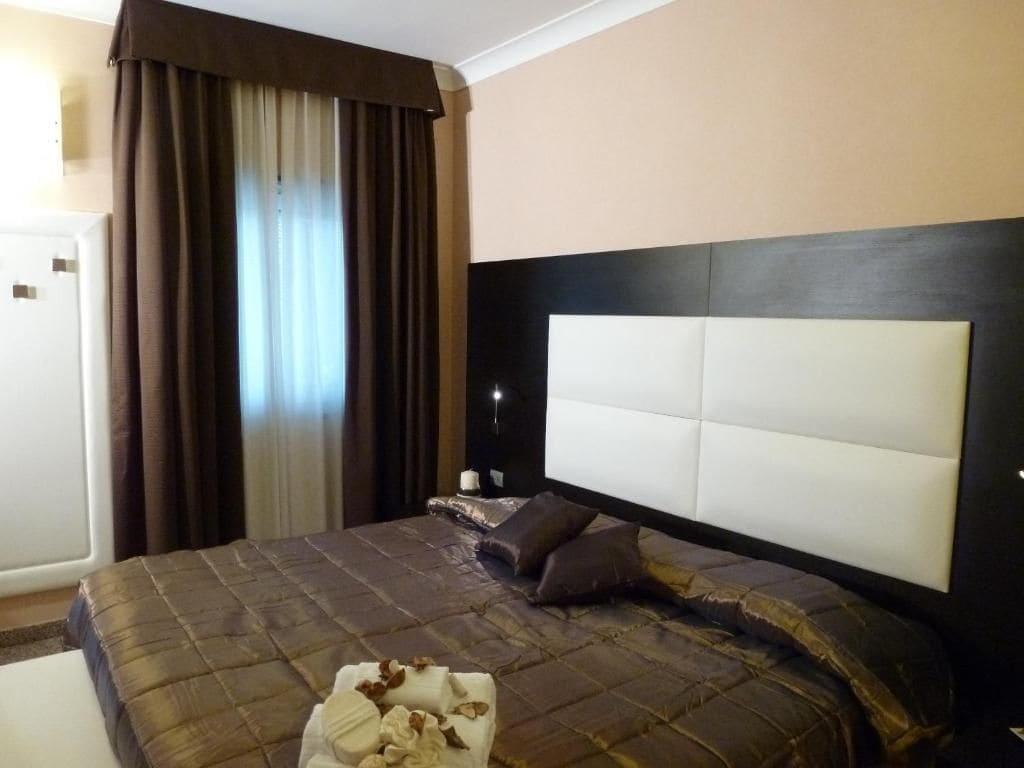 A hotel room with a large bed, a headboard, a nightstand, and a window with curtains.
