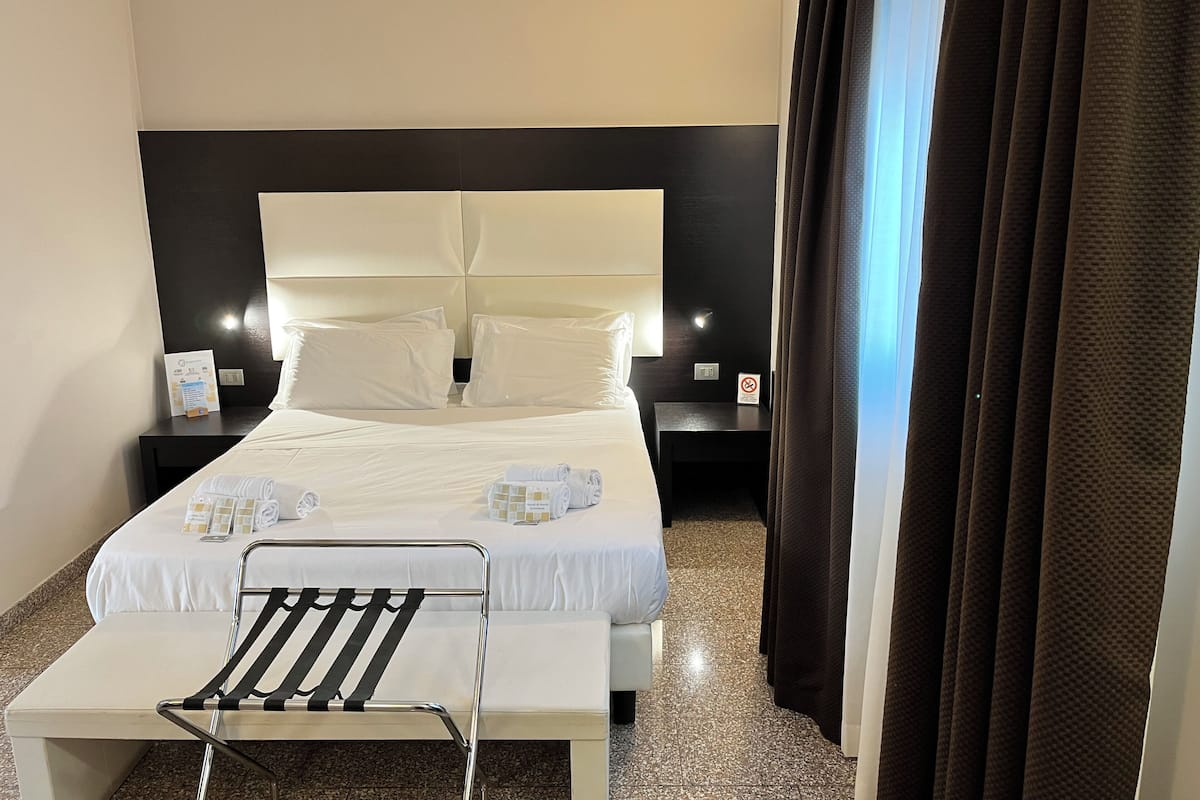 A hotel room with a large bed, a bedside table, a chair, and a nightstand.