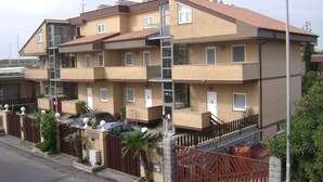 A multi-story residential building with balconies, a gated entrance, and a parking area. - E H SUITES ROME AIRPORT (Fiumicino)