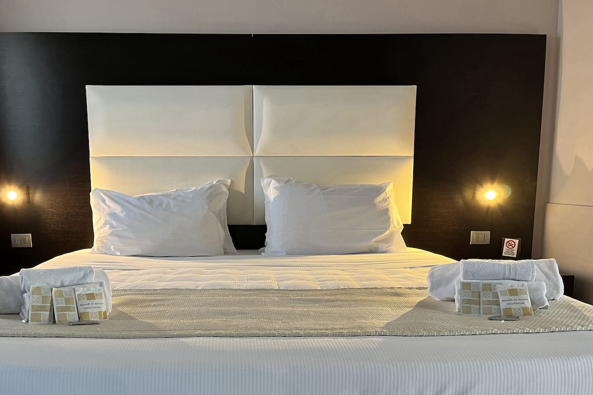 A neatly made bed with pillows, a folded towel, and a small card on the bed.