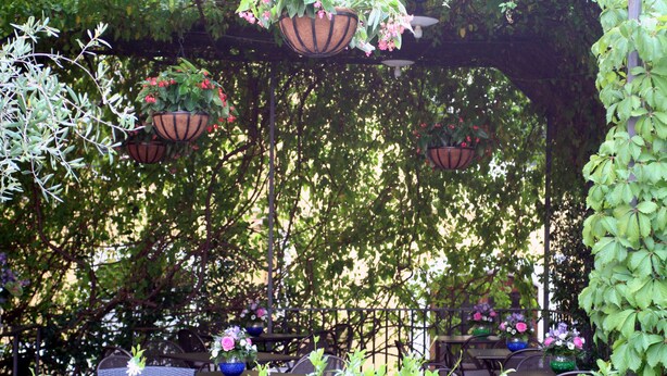 An outdoor seating area with tables and chairs, surrounded by hanging planters with flowers. - Hotel Charleston (Spoleto)