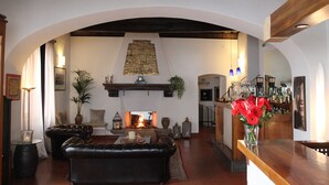 A cozy living room with a fireplace, leather sofa, and a bar area with a vase of red flowers. - Hotel Charleston (Spoleto)