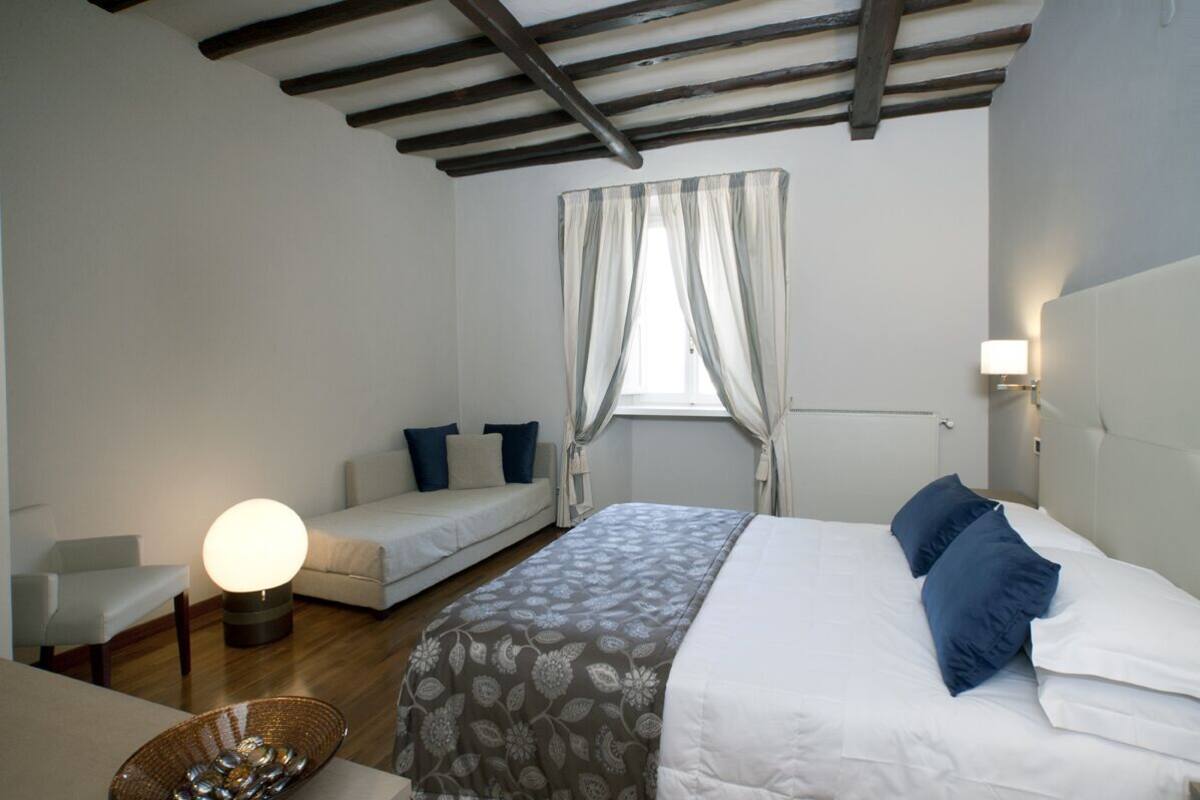 Un dormitorio con cama, sofá, mesita de noche, lámpara y ventana con cortinas.