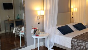 A bedroom with a bed, bedside lamps, a bedside table with a bottle and glasses, a mirror, and a television on the wall. - Hotel Charleston (Spoleto)