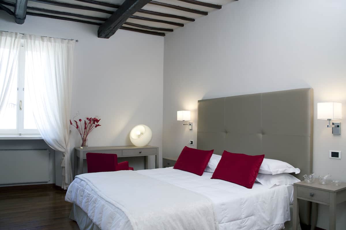 Una habitación de hotel con cama, mesitas de noche, escritorio y ventana con cortinas.