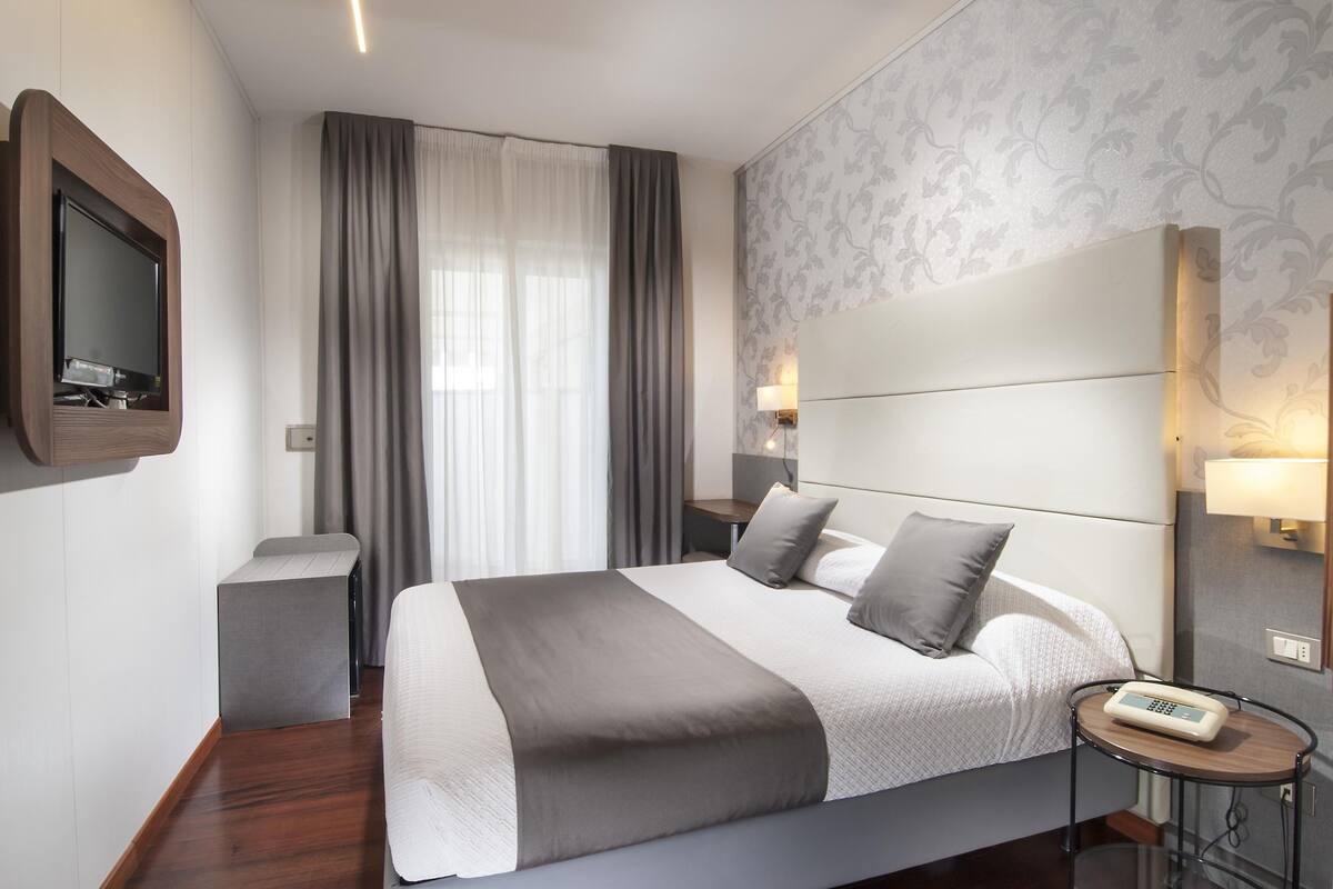 Ein modernes Hotelzimmer mit einem großen Bett, Nachttischlampen, einem Fernseher und einem kleinen Nachttisch.