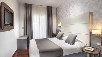 Una habitación de hotel moderna con una cama grande, lámparas de noche, un televisor y una mesita de noche.