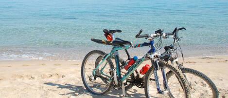 A bicycle parked on a sandy beach with clear blue water in the background.