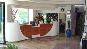 A reception area with a curved reception desk, a large vase with flowers, and a staircase in the background. - Hotel Artide (Rimini)