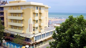 A hotel with multiple balconies and a pool area, overlooking a beach with umbrellas. - Hotel Artide (Rimini)