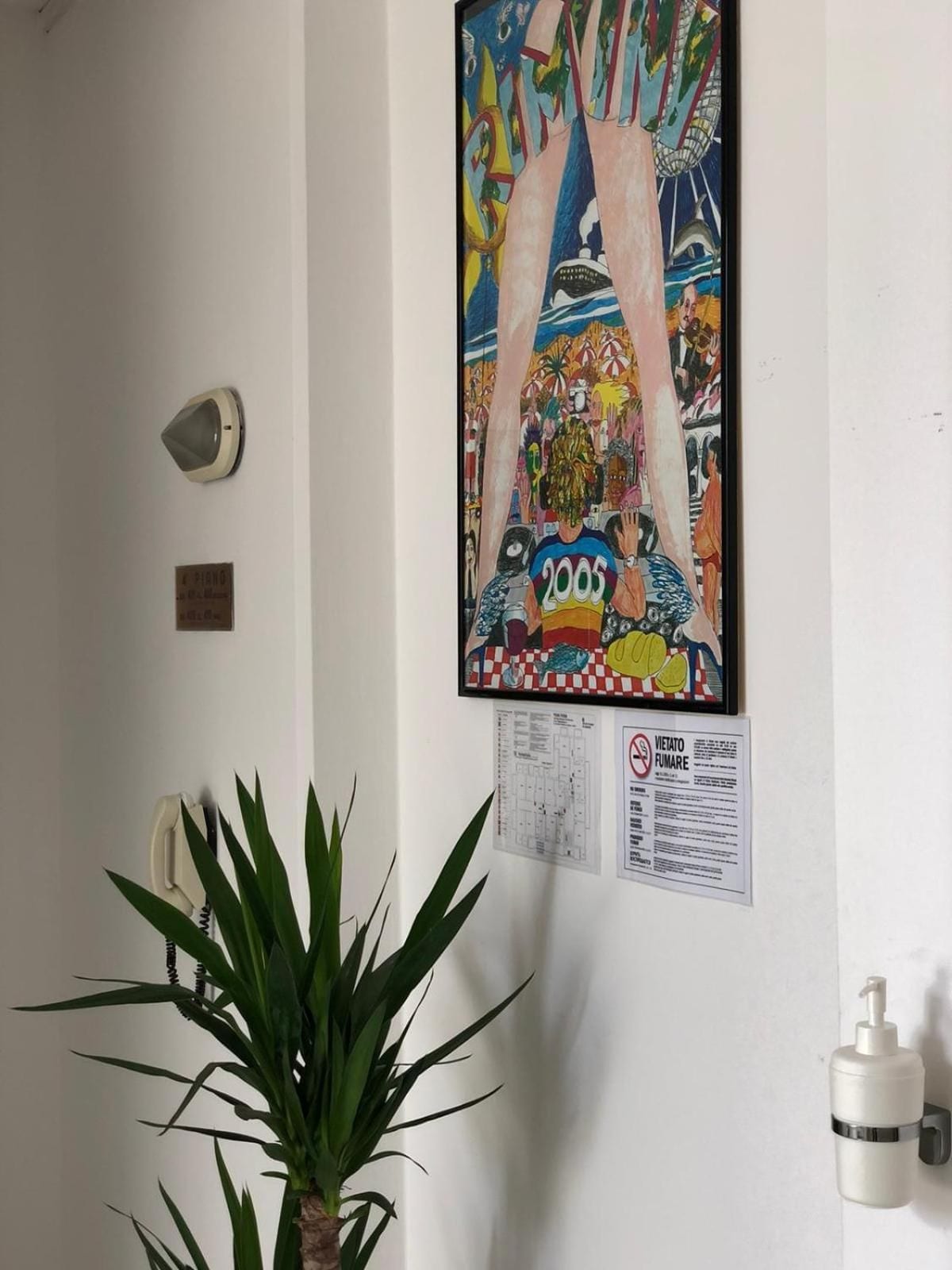 A wall with a colorful painting, a potted plant, a wall-mounted light, and a no-smoking sign.