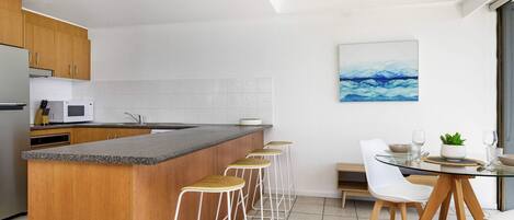 Una cocina moderna con una isla central, taburetes de bar, una mesa de comedor con sillas y un cuadro en la pared.