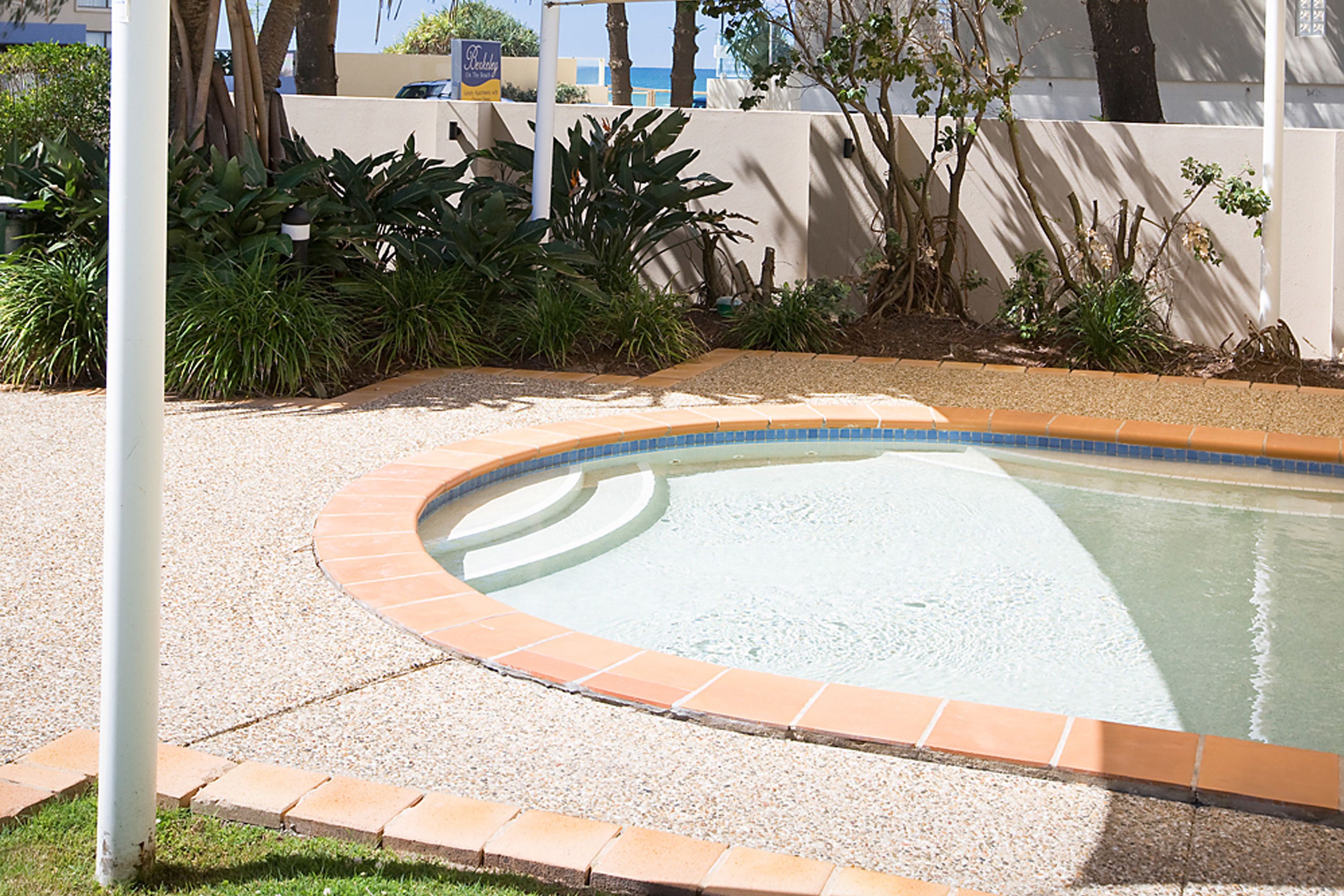 Una piscina de borde curvo, rodeada por una zona de grava y un bajo muro de ladrillo.
