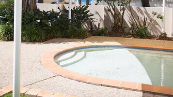 Una piscina de borde curvo, rodeada por una zona de grava y un bajo muro de ladrillo.