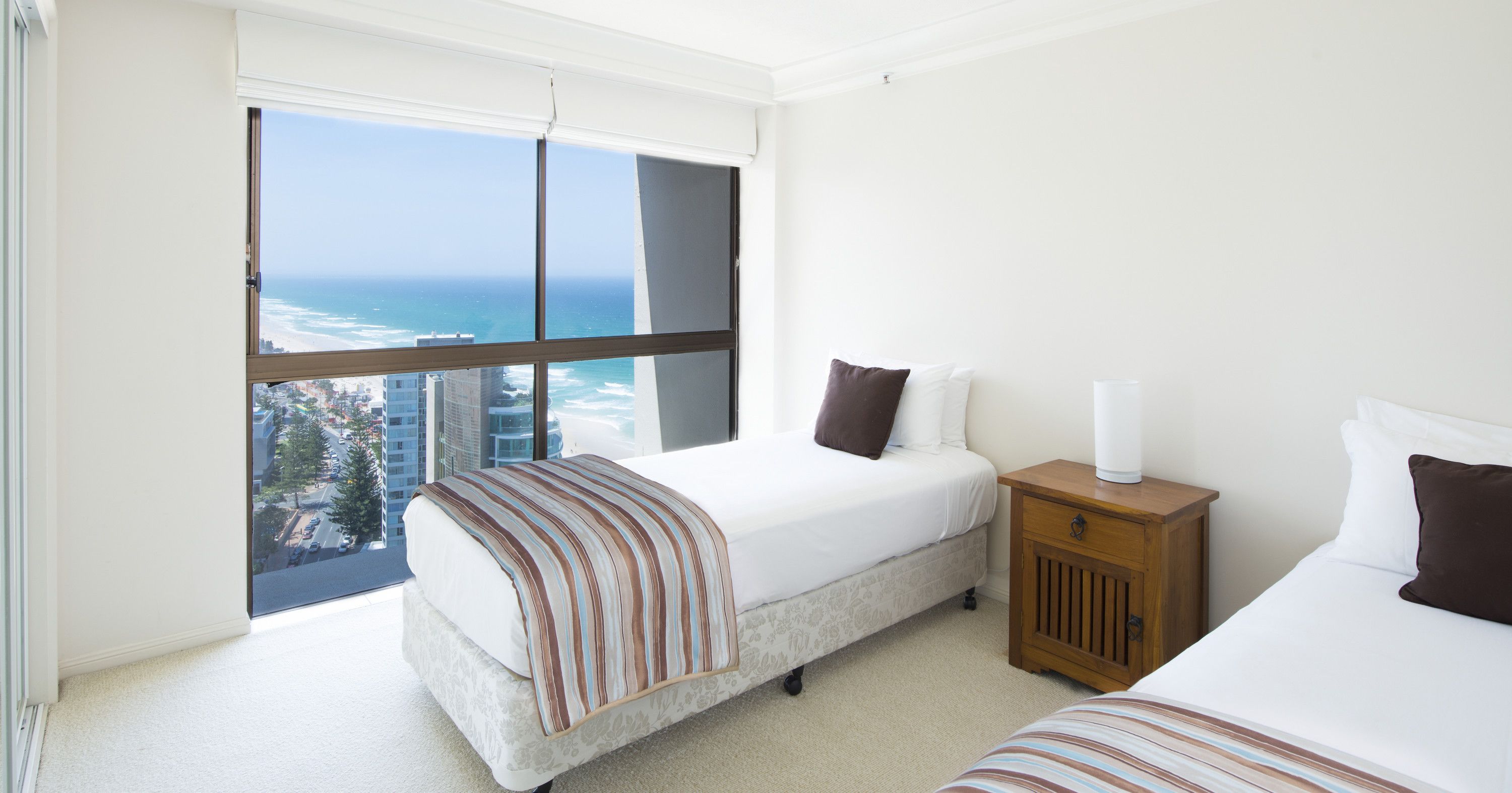 A hotel room with a large window offering a view of the ocean and cityscape.