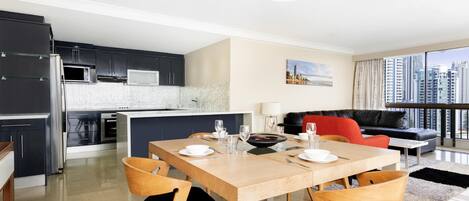 A modern kitchen with dark cabinets, a white island, and a dining area with a wooden table and chairs.