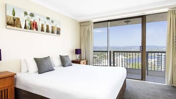 Ein Hotelzimmer mit einem großen Bett, einem Nachttisch, einem Gemälde und einem Balkon mit Blick auf die Stadt.