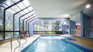 Una piscina interior amb parets de vidre transparents, un sol de fusta i baranes metàl·liques.