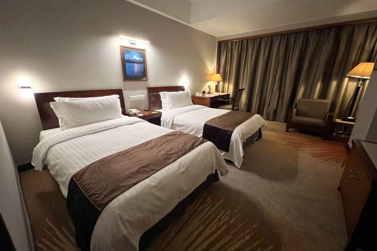 Habitación de hotel con dos camas, un escritorio, una silla, una lámpara y un cuadro en la pared.