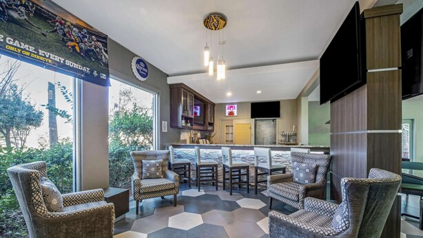 Un área de estar moderna con piso de patrón hexagonal, sillones de mimbre y una zona de bar con televisión.