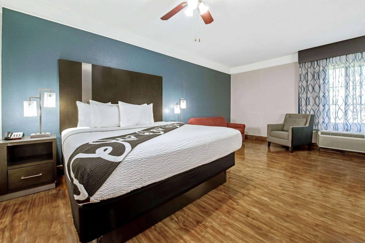 A hotel room with a large bed, a desk with a phone, a chair, and a window with curtains.