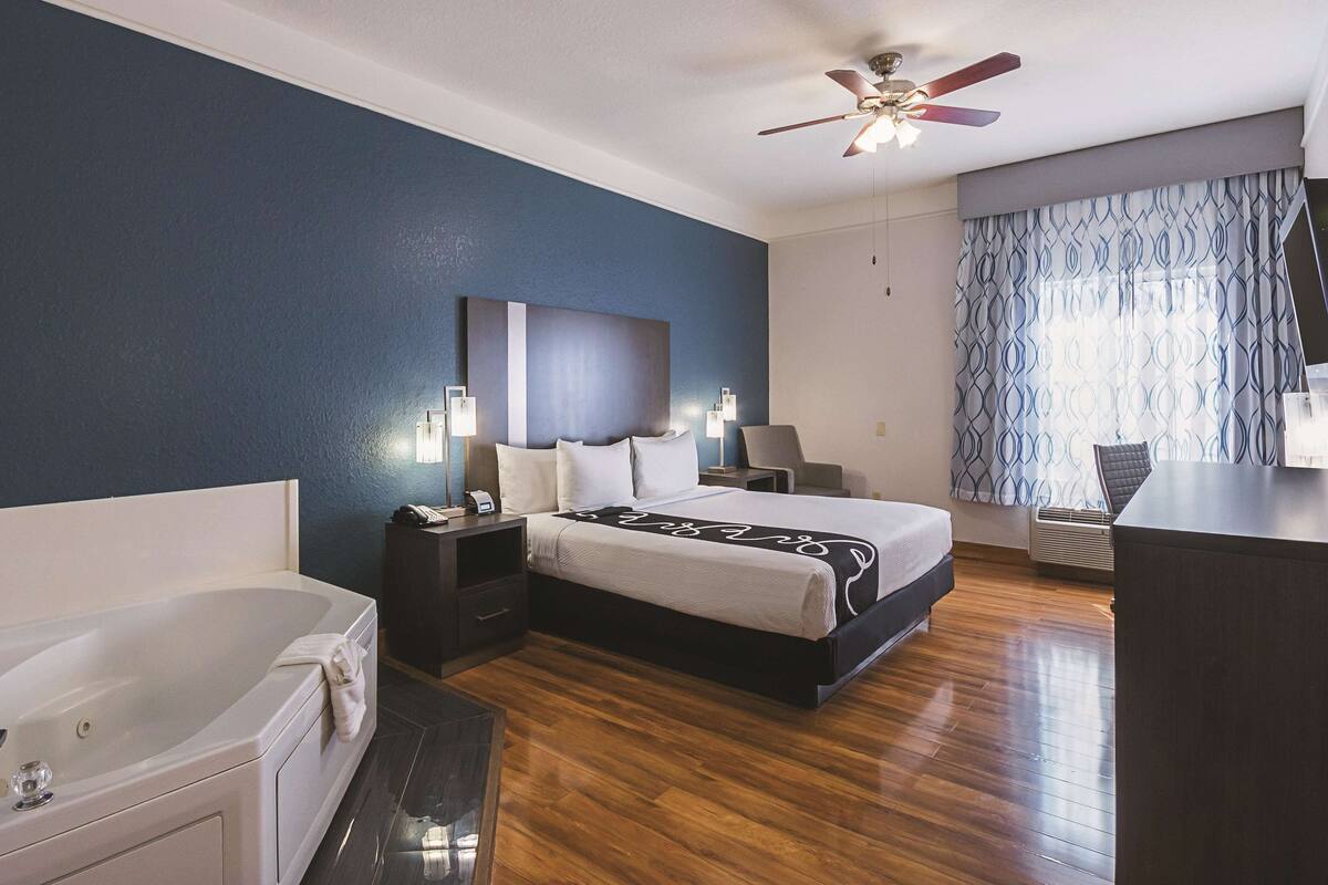 A modern hotel room with a large bed, a separate bathroom, a ceiling fan, and a patterned curtain.