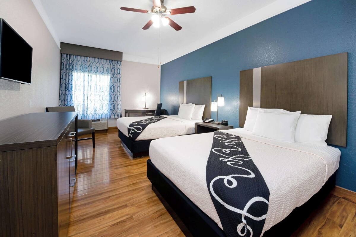 A hotel room with two beds, a desk, a ceiling fan, and a TV.