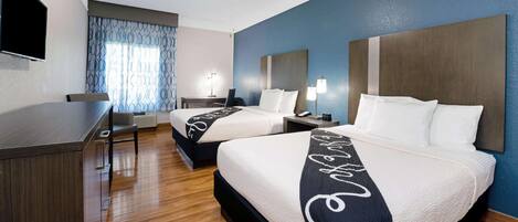 A hotel room with two beds, a desk, a ceiling fan, and a TV.