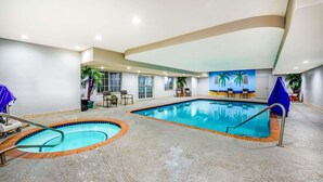 Una piscina interior con dos zonas separadas, un techo con iluminación empotrada y un mural de palmeras en la pared.