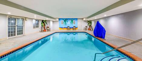 A swimming pool with a tiled edge, a blue mural with palm trees, and a blue chair.