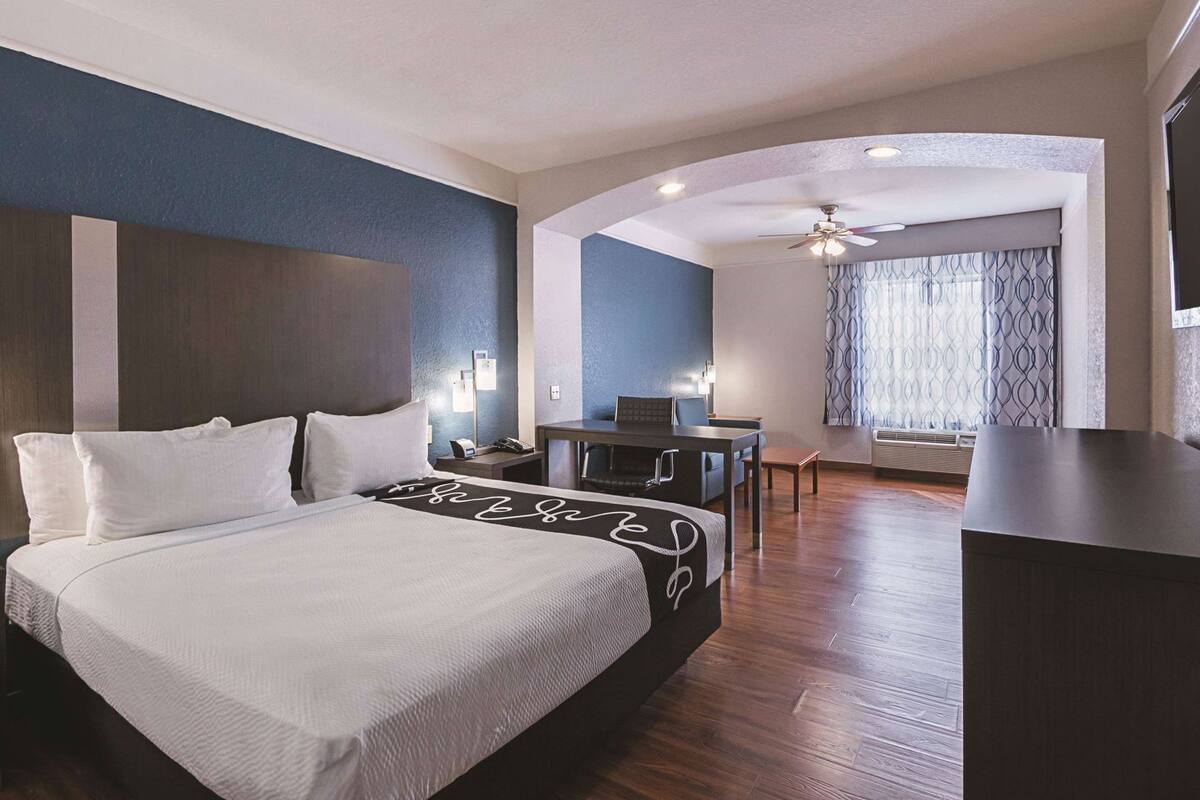 A hotel room with a bed, desk, chair, and a view of the outside.