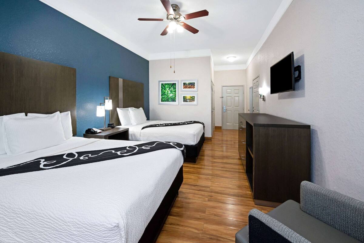 A hotel room with two beds, a ceiling fan, a TV, and a desk.