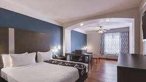 Habitación de hotel con cama, escritorio, silla, ventilador de techo y ventana con cortinas.
