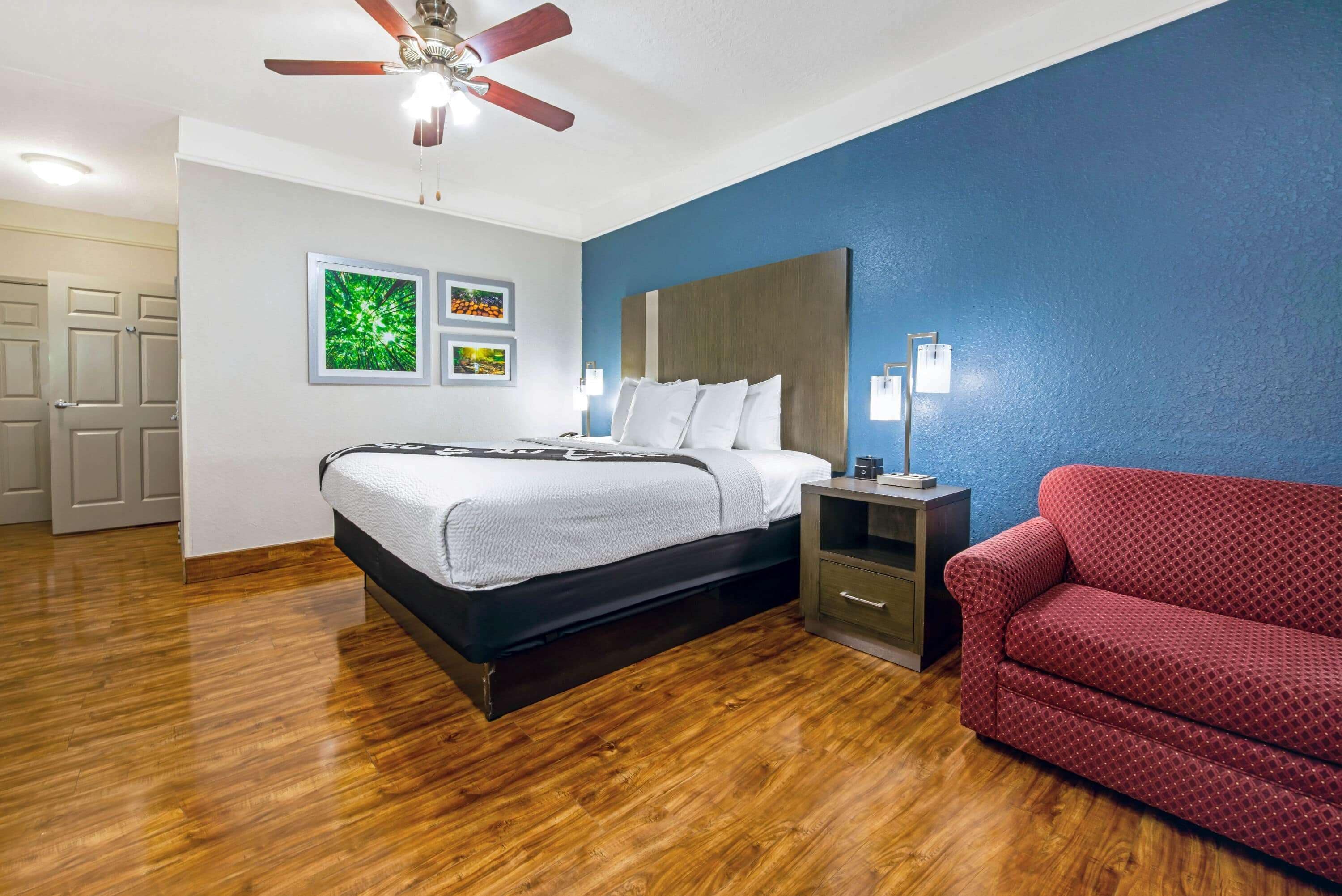 A bedroom with a bed, a red couch, a ceiling fan, and wall art.