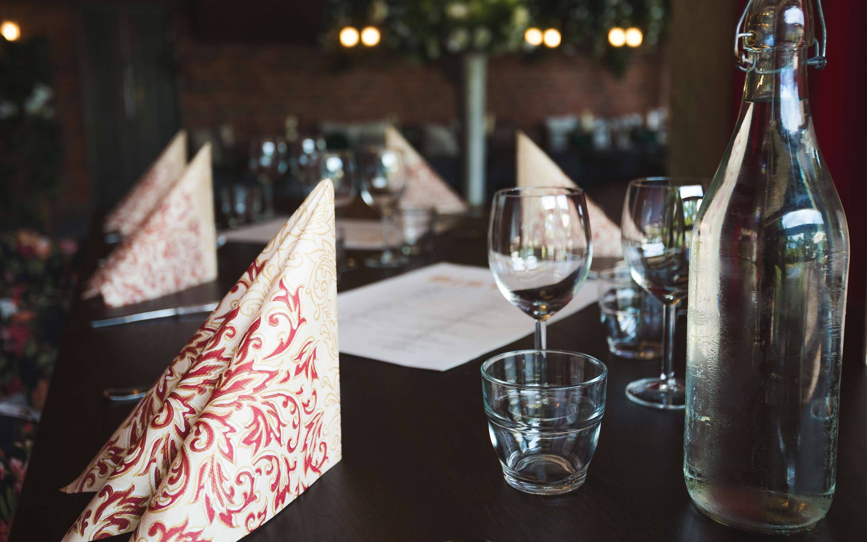 A dining table set with a patterned napkin, a clear glass bottle, and wine glasses.