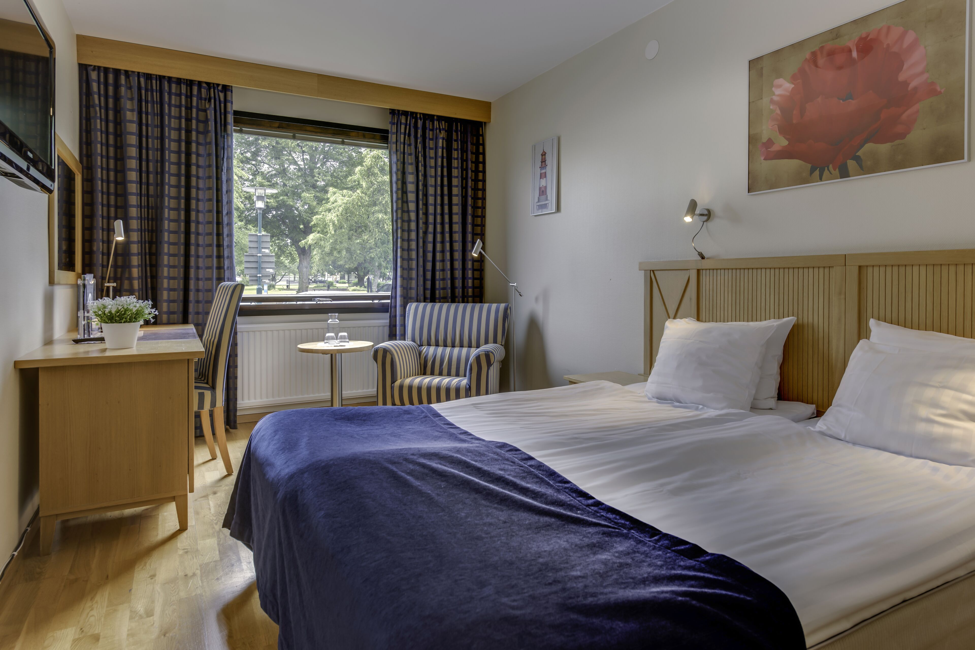 A hotel room with a bed, a desk, a chair, a small table, and a window with curtains.