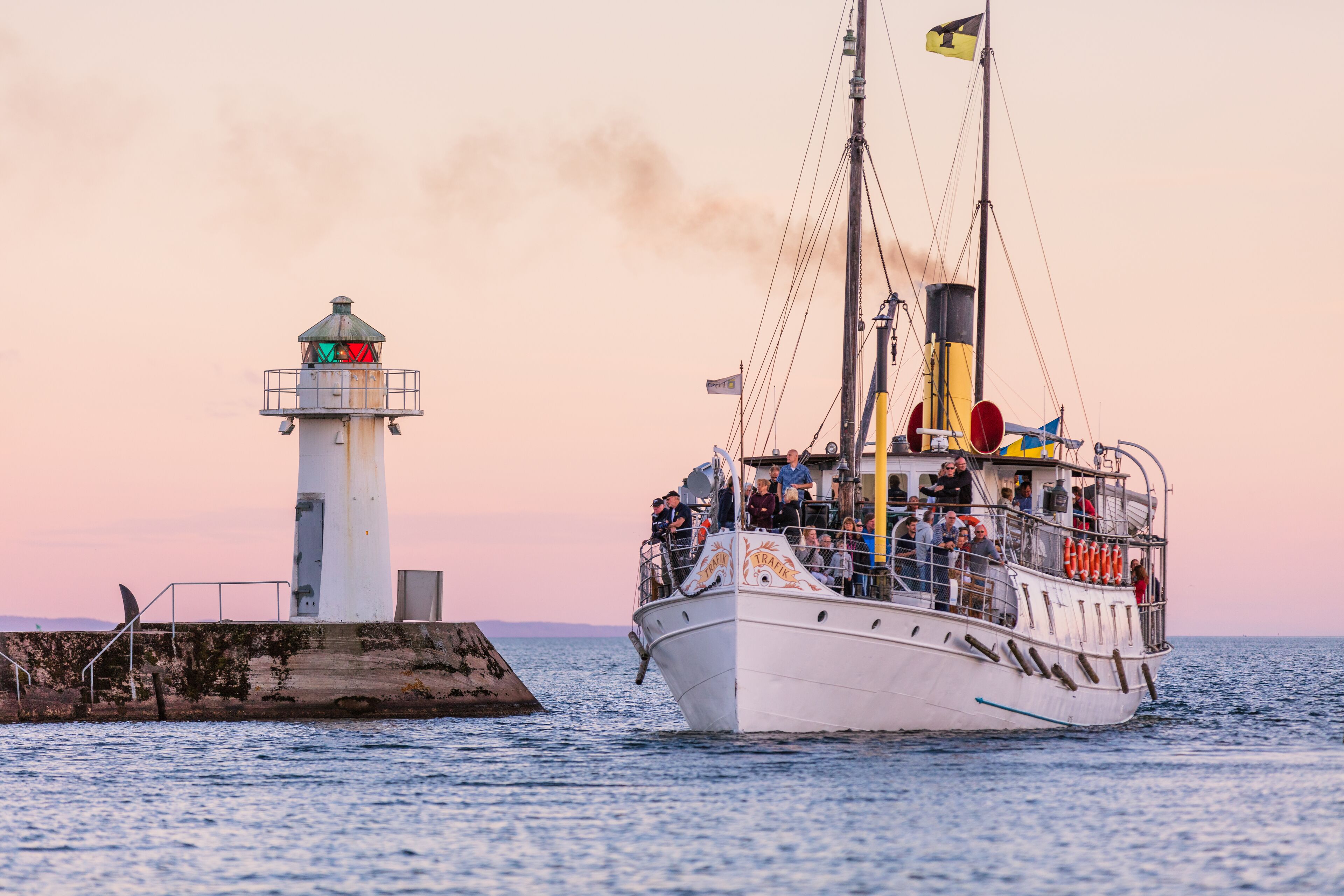 A boat with passengers and a lighthouse in the background.
