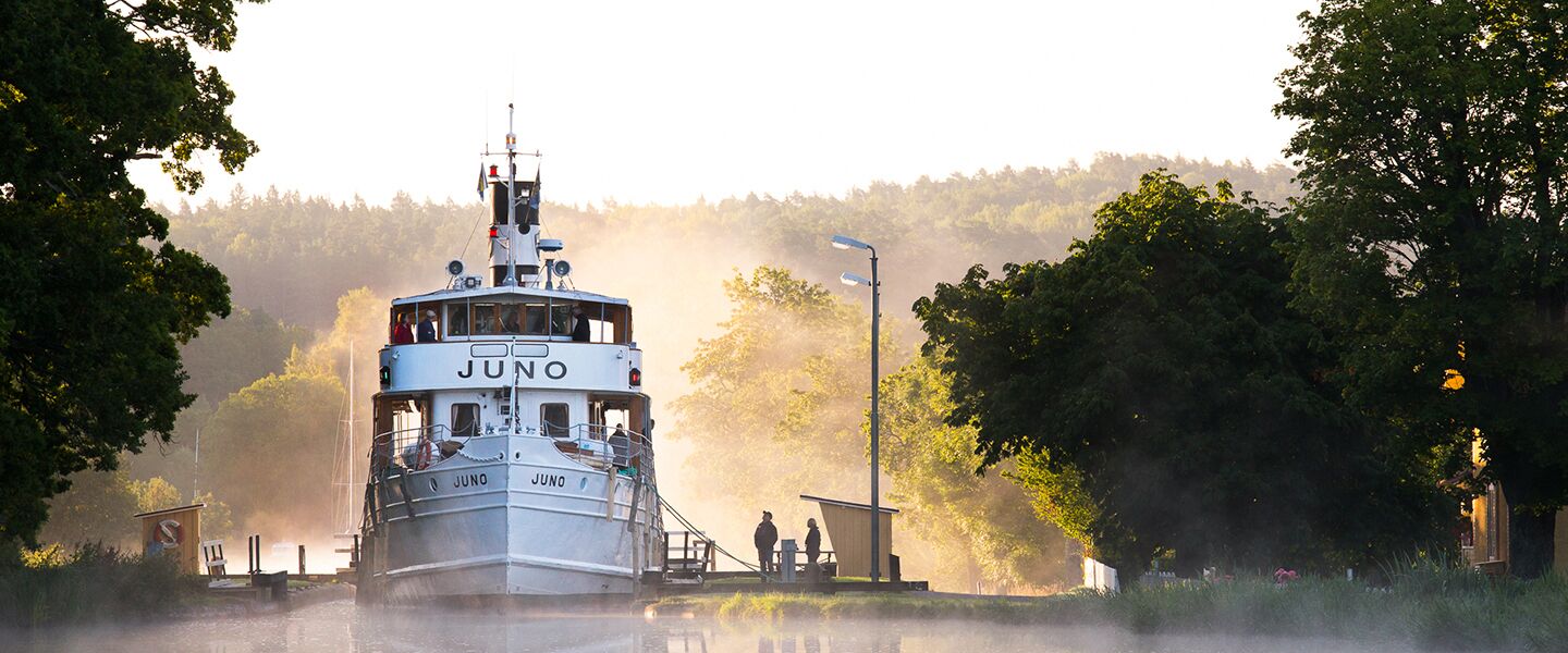 A boat named Juno docked at a pier with a misty forest backdrop.