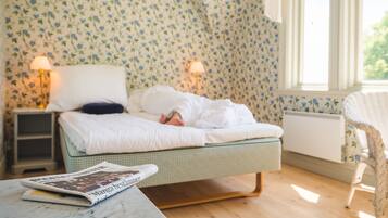 A bedroom with a bed, two bedside lamps, a chair, and a table with a magazine.