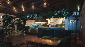 Ein gemütlicher Innenbereich mit Holztisch, grünen Sitzstühlen, einer Bar mit Kasse und hängenden Pflanzen.