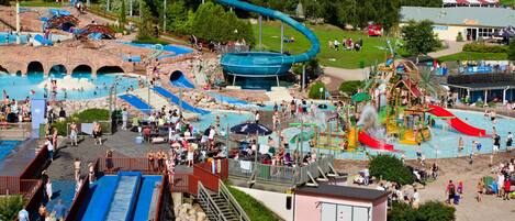 A water park with multiple slides and pools, surrounded by trees and a building in the background.