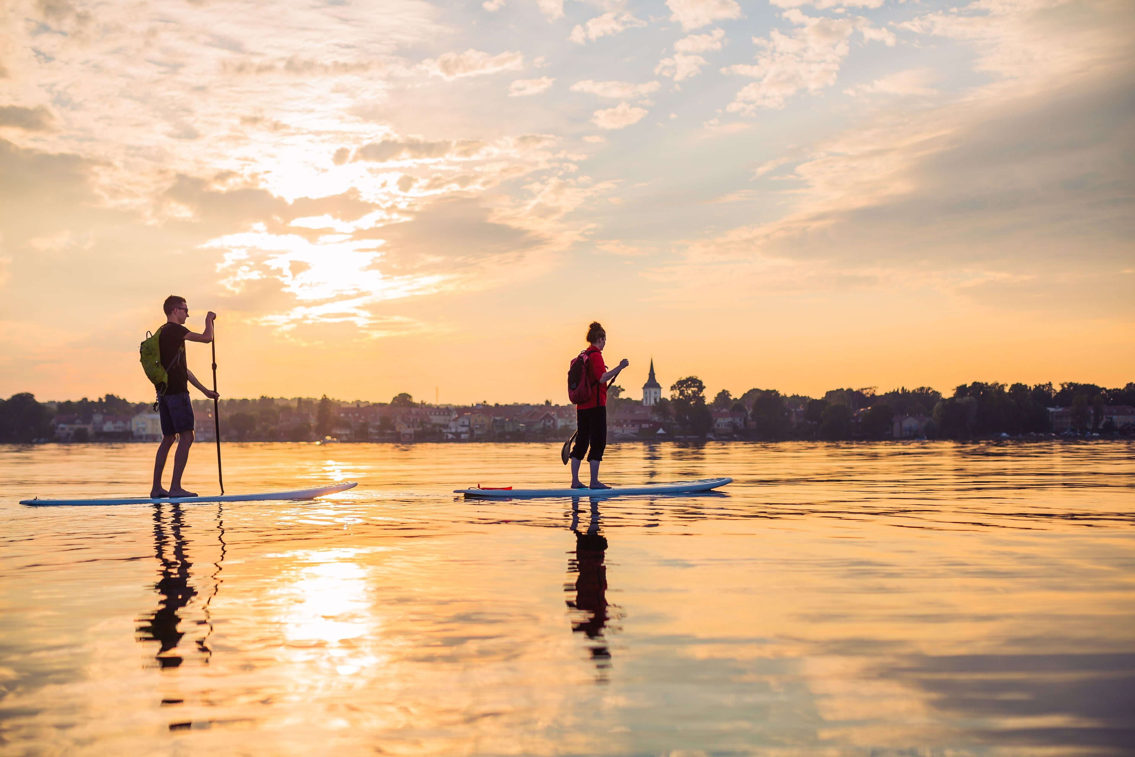Dos personas haciendo paddleboard en aguas tranquilas durante el atardecer.